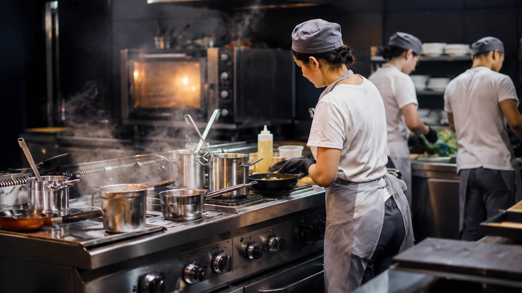 Brigata al lavoro in una dark kitchen professionale con fornelli e pentole in acciaio durante la preparazione degli ordini