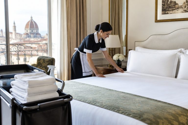 Cameriera ai piani rifà il letto in una camera d'albergo luminosa con asciugamani sul carrello