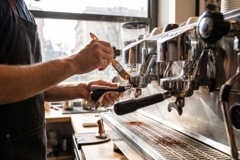 Barista che pulisce il gruppo erogazione di una macchina espresso professionale in un bar